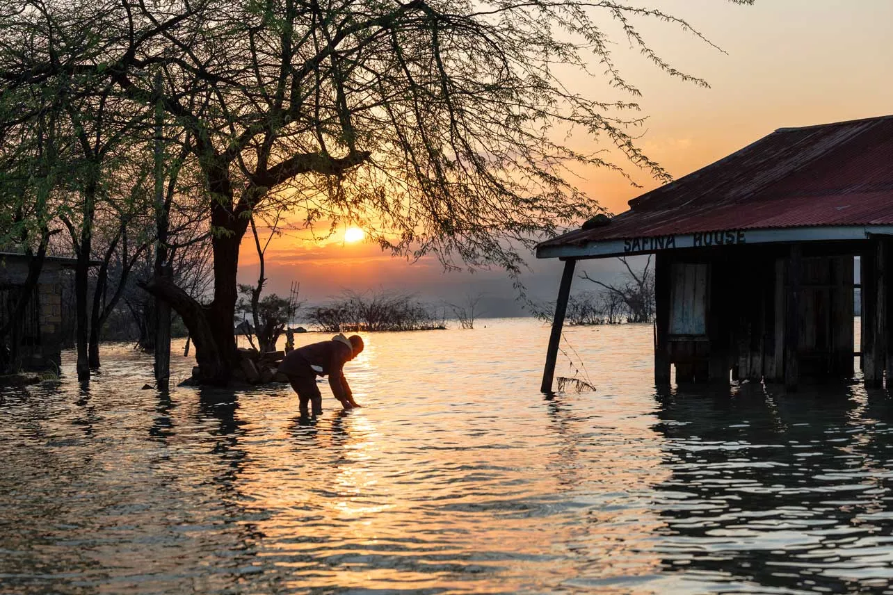 Un atardecer. Se ve a un hombre agachado en el agua y una casa inundada.