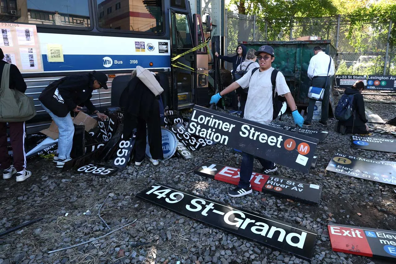 Una persona carga con una señal antigua del metro de Nueva York.